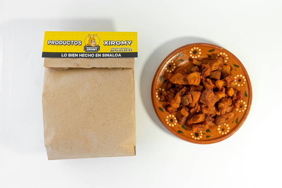 A smiling woman holding her orange tabby cat while pointing at its full food dish